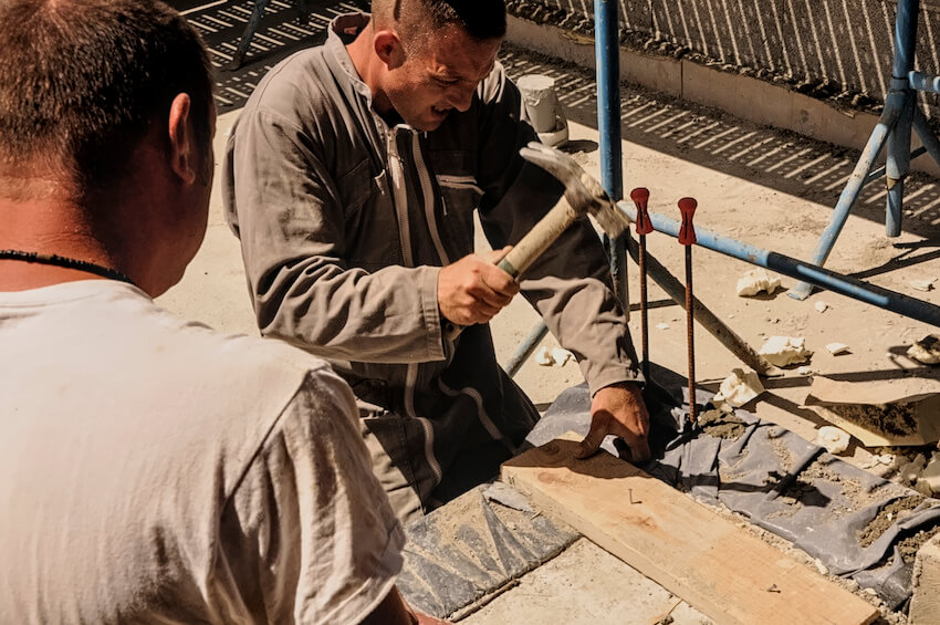 Deux maçons aux travail. L'un clou une planche pour un coffrage béton.